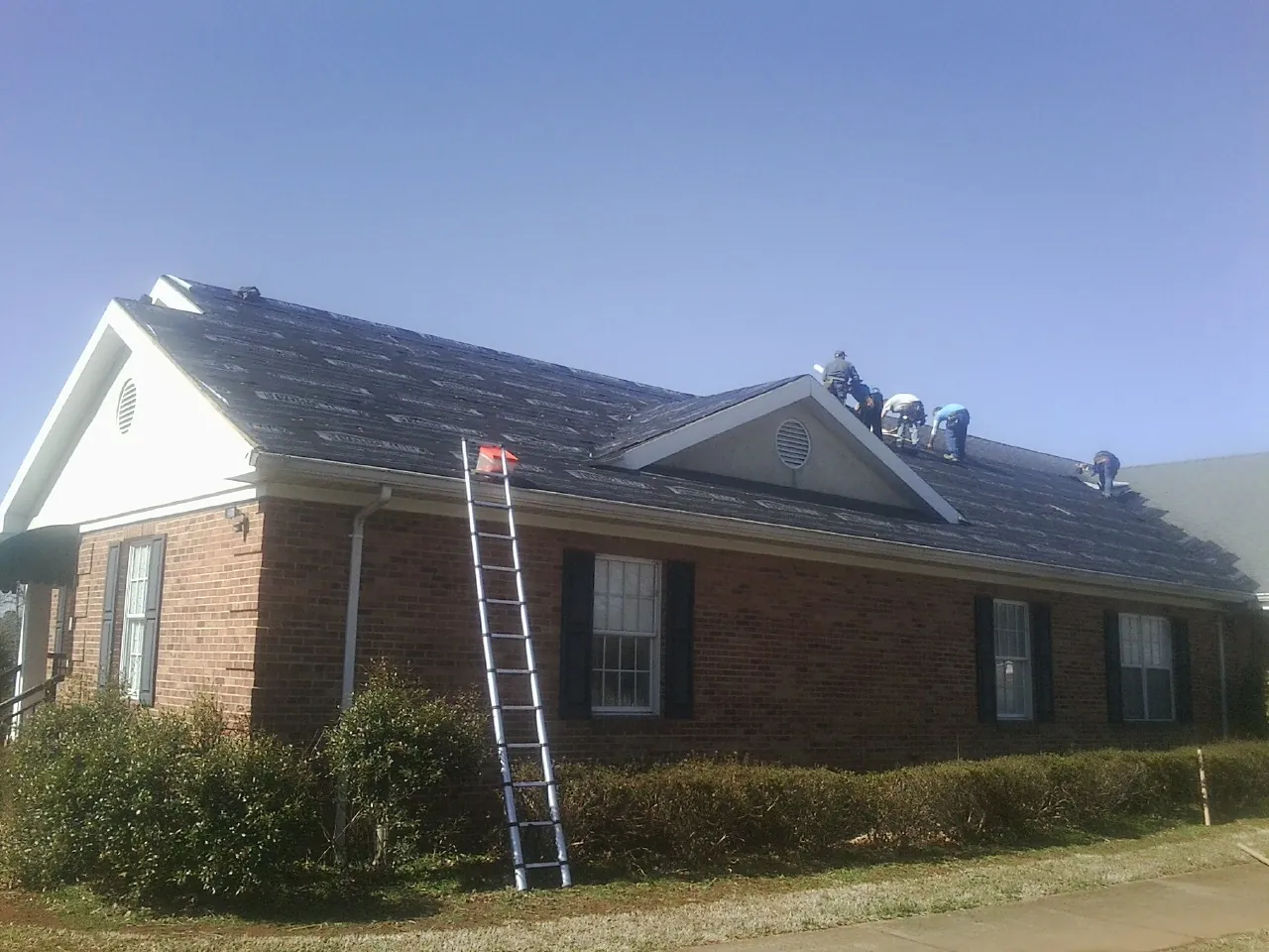 Crew tearing shingles off a brick ranch roof with a ladder set — Metal Roof Repair work by our crew in Ridgefield
