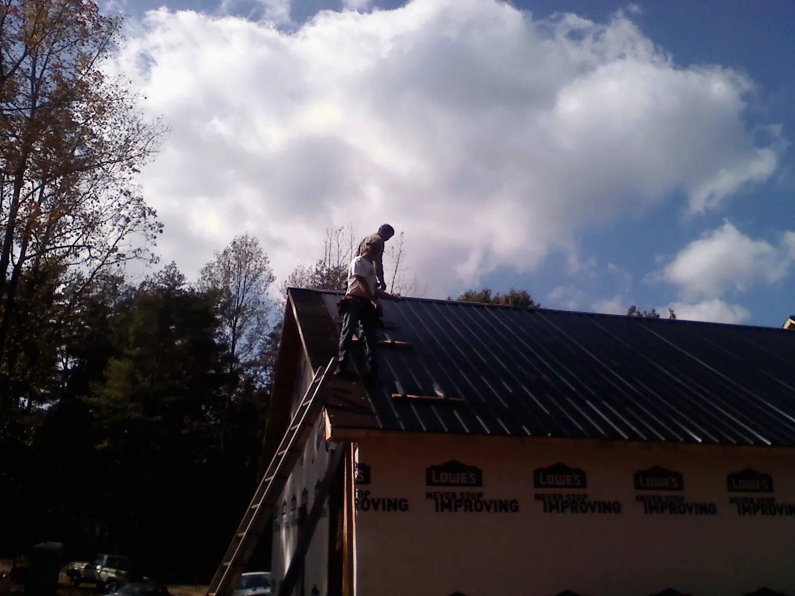 Roofer fastening dark metal panels high against a cloudy sky, from a Roof Inspection job in Ridgefield